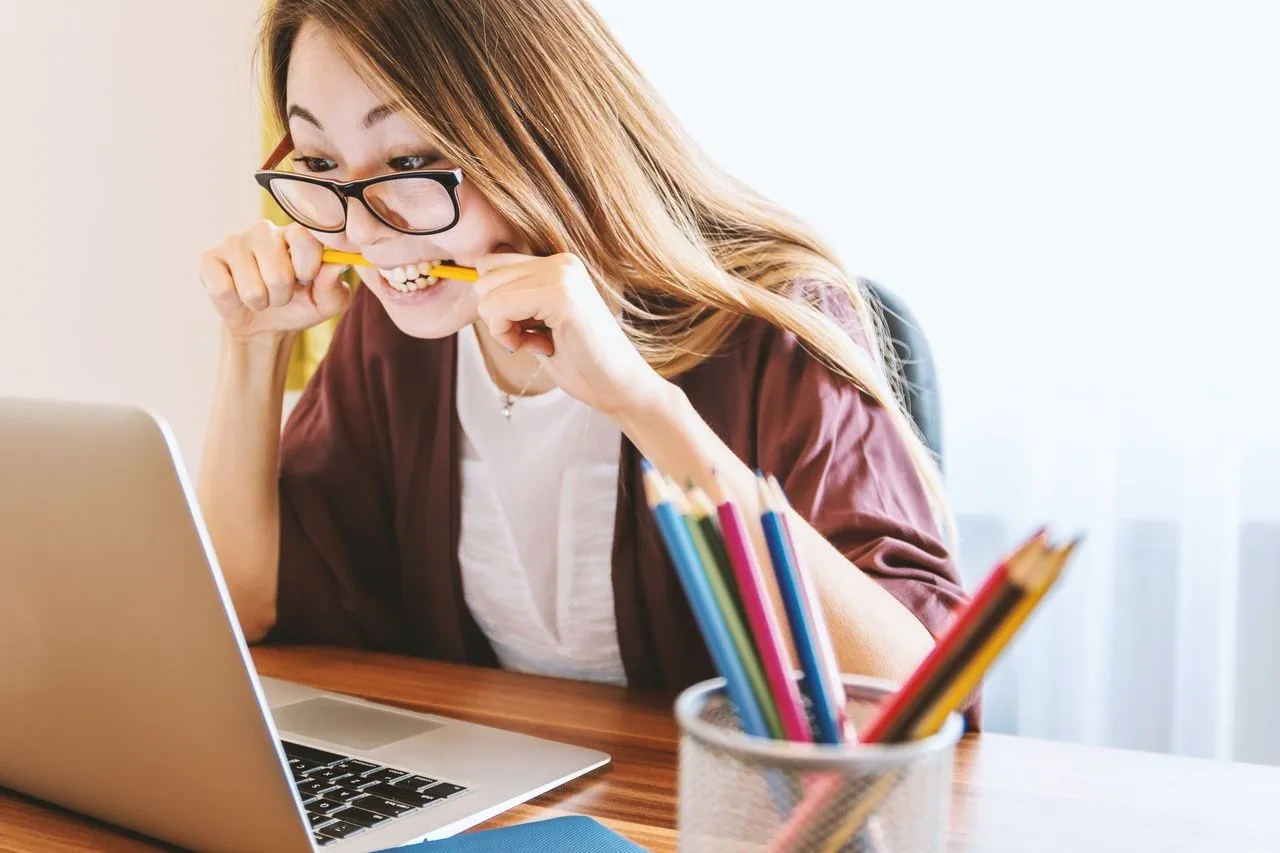 an angry woman who bites her pencil and looks toward to her laptop