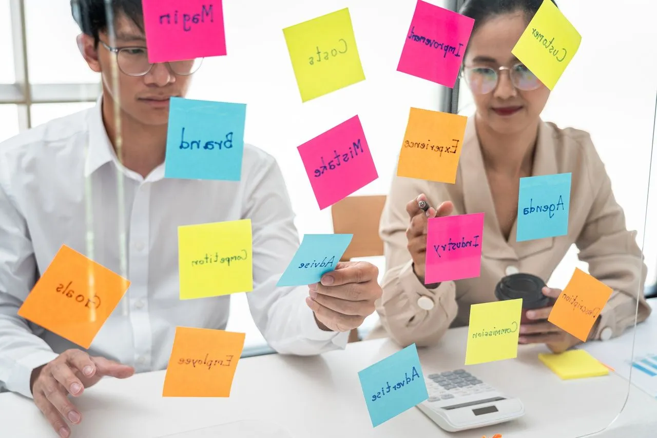 two people holding and pointing keywords that are written on the sticked notes